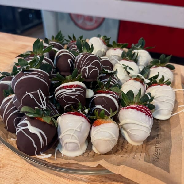 A platter of chocolate-dipped strawberries, some with white chocolate drizzle, on a paper-lined tray.
