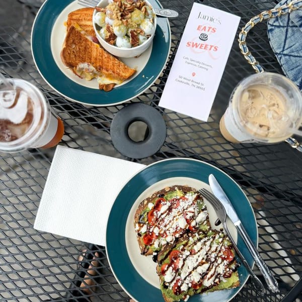 Overhead view of grilled cheese, fruit salad, avocado toast, and drinks on a cafe table.