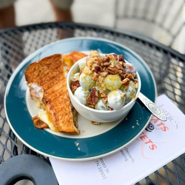Grilled cheese sandwich and a bowl of grape salad with pecans and brown sugar on a patio table.