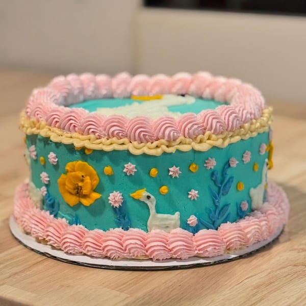 A whimsical teal cake with pink and yellow frosting, featuring a white goose and yellow flower.