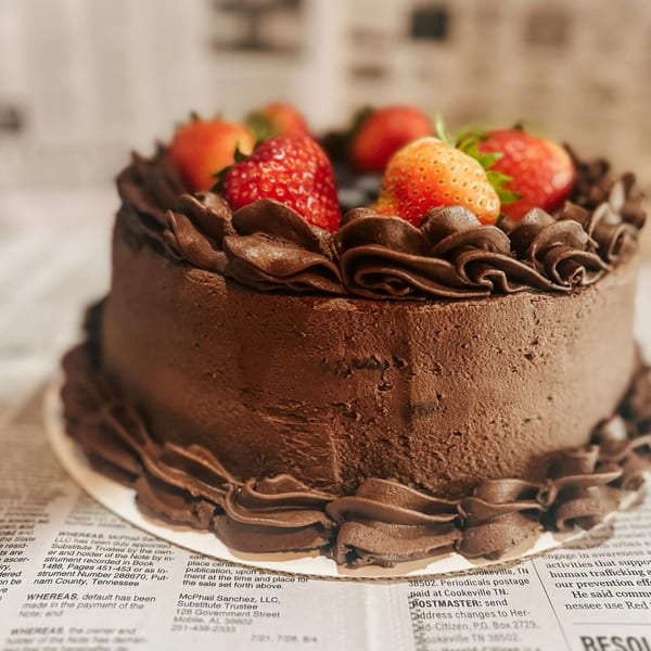A rich chocolate cake with chocolate frosting swirls and fresh strawberries on top, on a newspaper.
